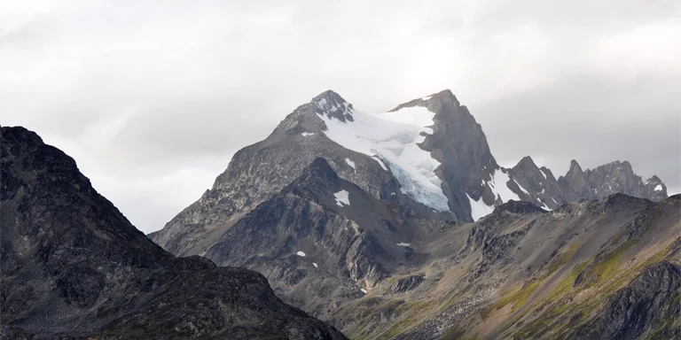 Towering peaks breach wispy clouds above rocky valleys in this sweeping vista of the wild Cerro Vinciguerra massif in Argentina's Tierra del Fuego, its scenic yet foreboding Patagonian landscape revealing rugged beauty under a partially overcast sky