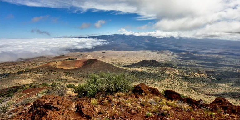 Mauna Loa's immense slopes stretch endlessly into the distance, its subtle forms emerging from and remerging into drifting clouds along the pacific horizon