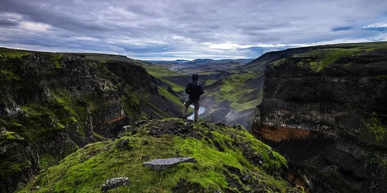 Backpacking in Iceland: A backpacker standing on a scenic mountain, looking at a green valley