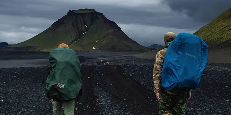 Two hikers with backpacks trek across a dirt road on Iceland's scenic Laugavegur Trail, surrounded by rugged volcanic terrain