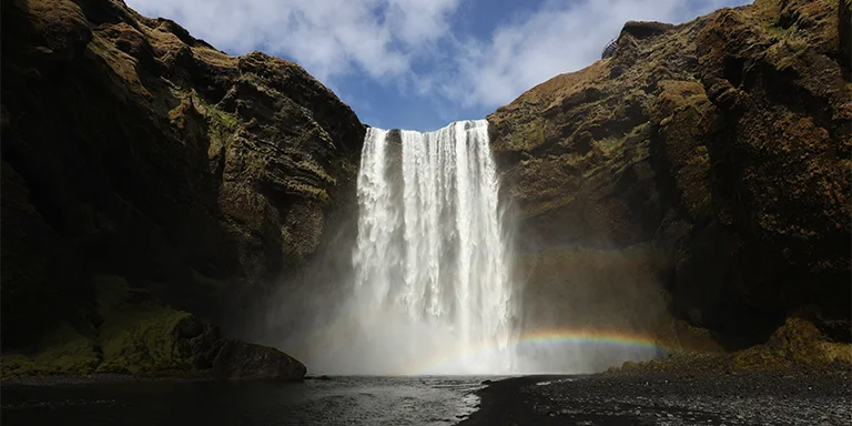 The mighty Skógafoss waterfall cascades down a cliffside under bright blue skies in Skógar, Iceland