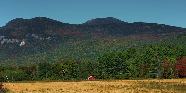 A picturesque red house overlooks a sunny valley surrounded by the fall foliage of Maine's scenic Grafton Notch