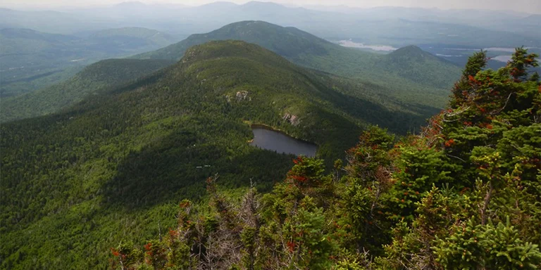 The Appalachian Trail traverses a ridge overlooking the vivid Horns Pond and lush green mountains of Maine