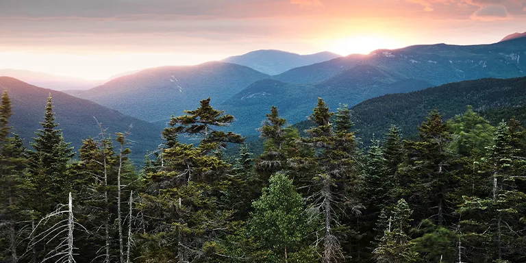 Dramatic sunset silhouettes the rugged peaks of the White Mountain National Forest in New Hampshire, viewed from an overlook along the scenic Kancamagus Pass