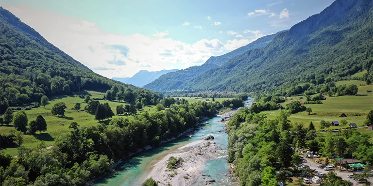 A lush green tree lot by a crystal clear blue river in Slovenia