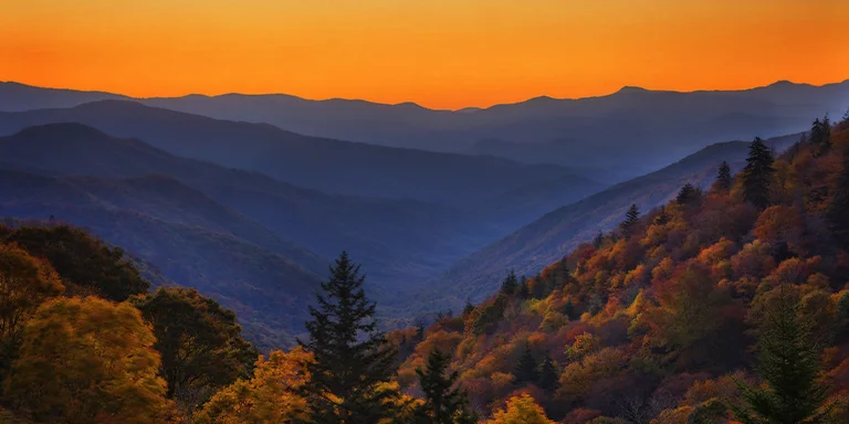 A stunning photo capturing the beauty of a colorful Smoky Mountain sunrise illuminating the layered mountain peaks and valleys below as morning fog blankets the landscape from the Oconaluftee Overlook in Great Smoky Mountains National Park