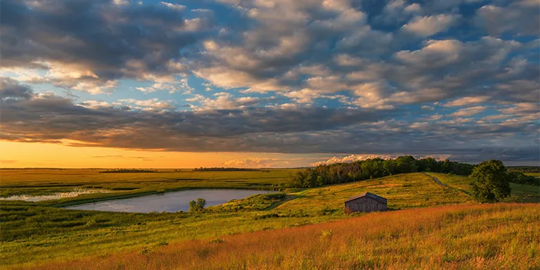 A quaint little house sits atop a grassy hill, bathed in the golden light of the setting sun at Horicon Marsh, Wisconsin