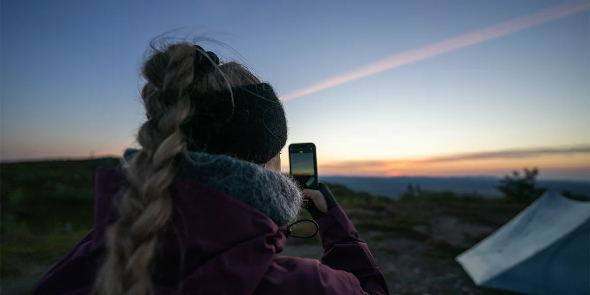 Backpacking in Finland: A female hiker taking a picture of the scenic sunset in Finland