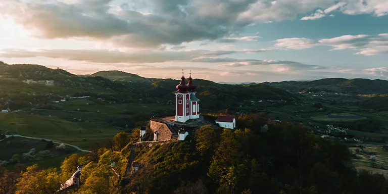 A stately brown and white building stands surrounded by lush green grass under brooding gray skies in the quaint Slovakian town of Banská Štiavnica