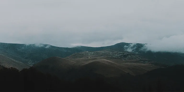 The jagged, rocky peaks of Muntii Tarcu enveloped by ominous clouds and fog, creating a mood of solitude and mystery in the bleak Romanian landscape