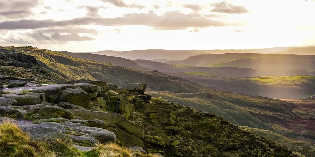 A picturesque landscape showcasing the rugged beauty of the Peak District in Castleton, UK, with rolling grassy hills dotted with rocky outcrops