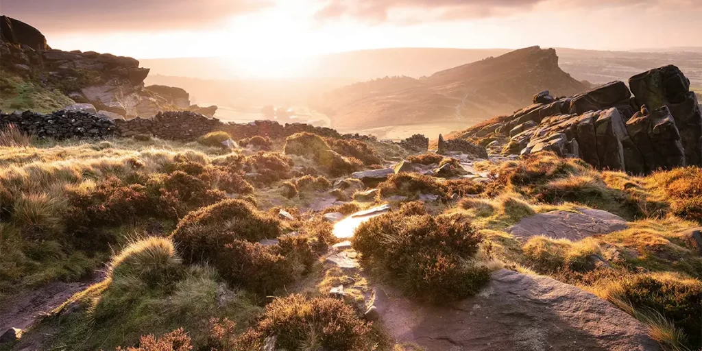 As the sun sets, its warm glow bathes the rugged, rocky terrain of The Roaches in Leek, UK