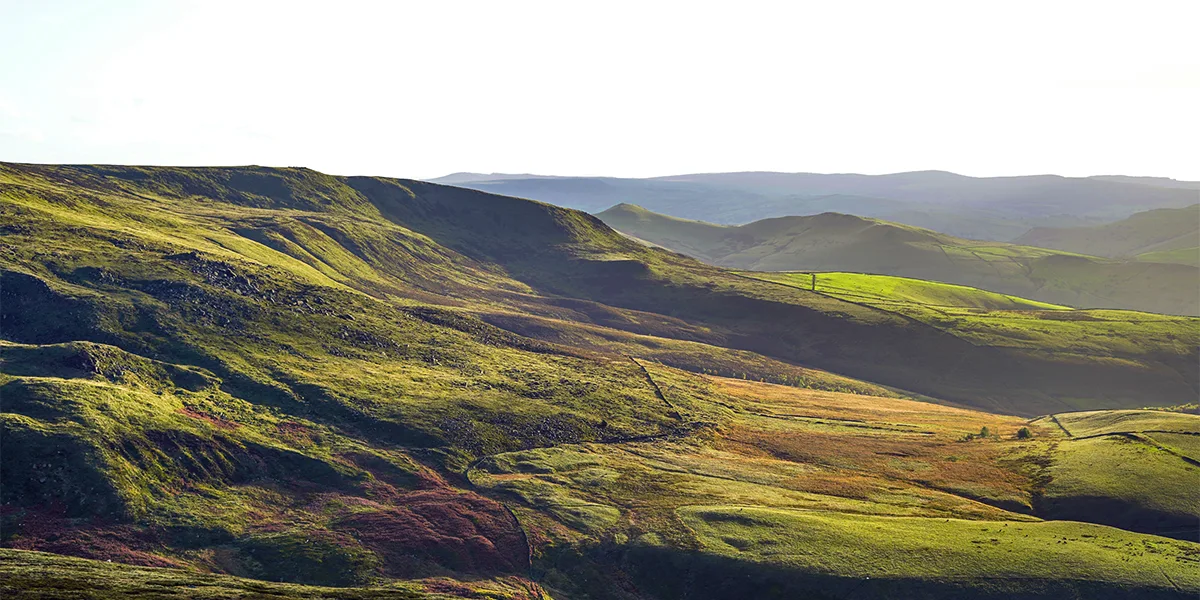 A scenic vista of rolling grassy hills and valleys in the picturesque Peak District of England