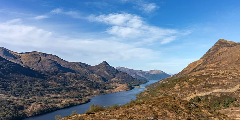 A breathtaking panoramic view of a tranquil lake surrounded by towering mountains in the scenic landscape of Kinlochleven, United Kingdom