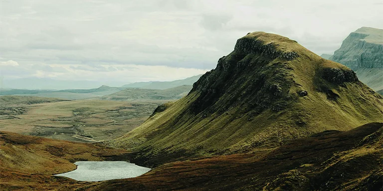 Majestic mountains with unique rock formations tower over tranquil small lakes, showcasing the surreal and beautiful landscape of Quiraing in Scotland