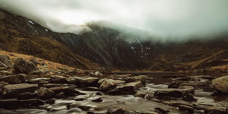 A tranquil river winds its way through a scenic valley surrounded by towering mountains in the picturesque Llyn Idwal area near Bangor, UK