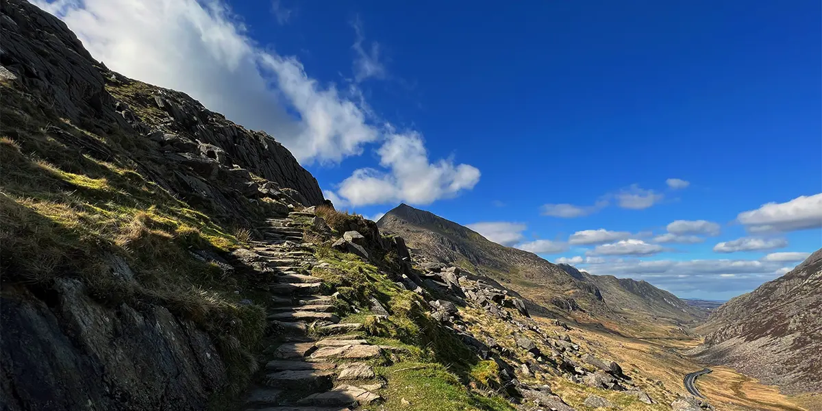 A winding stone path ascends a rugged mountainside in Snowdonia National Park, UK